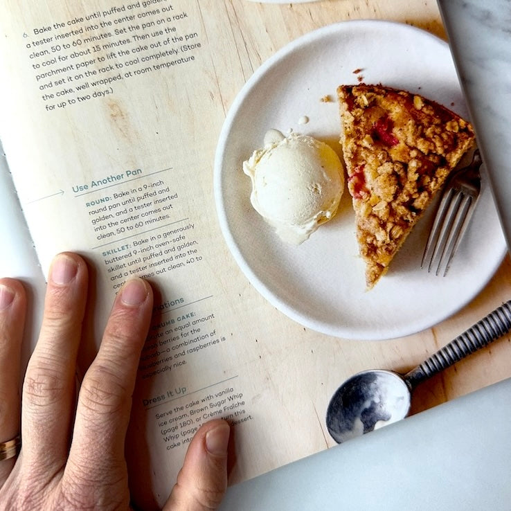 Hand over a cookbook showing a slice of delicious rhubarb cake with a side of ice cream.