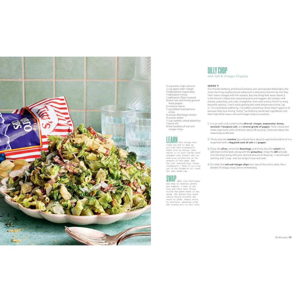 A vibrant salad on a plate with a spoon beside it, set against a green tiled background. Ideal for quick meals or fresh dinner ideas, it's accompanied by an open bag of chips. Explore simple recipes and cooking tips from "What To Cook When You Don't Feel Like Cooking" by Gneiss Spice.