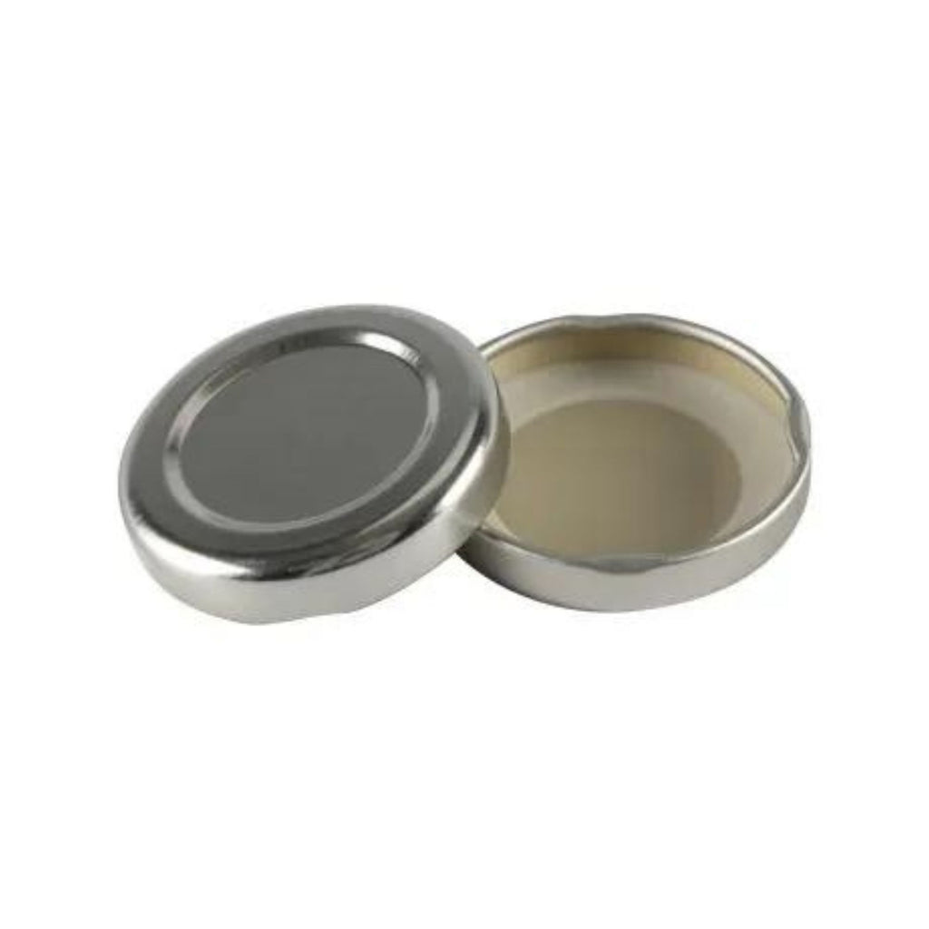 An unlabeled metal tin, designed by Gneiss Spice, features a detachable lid, slightly ajar to reveal the interior. The smooth, reflective exterior glimmers subtly, while the inside appears empty. Set against a plain white background, this piece is crafted without magnetic components for convenience.