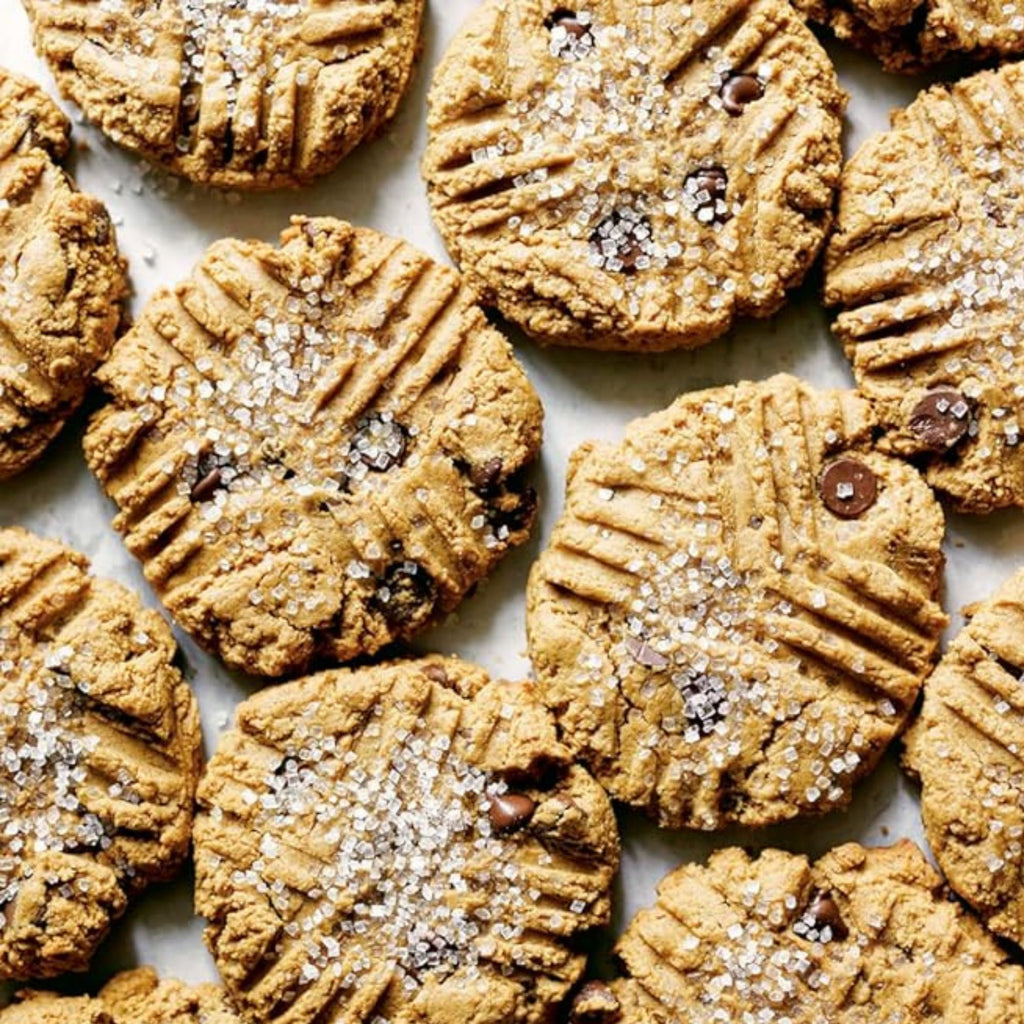 A batch of freshly baked cookies inspired by Zoë François' recipes from "Zoë Bakes Cookies: Everything You Need to Know to Make Your Favorite Cookies and Bars" by Gneiss Spice. These delightful treats are topped with sugar crystals and chocolate chips, each featuring a crisscross fork pattern on top, arranged closely on a light background.