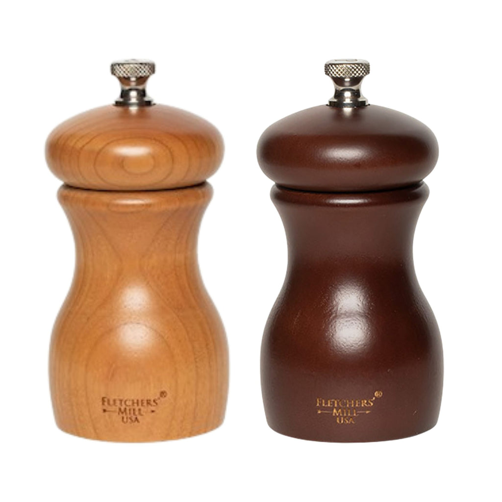 Two wooden mills from the Gneiss Spice Grinder Gift Set stand side by side, crafted sustainably. The mill on the left is light brown and the one on the right is dark brown, each topped with a silver knob and engraved at the bottom. These salt and pepper grinders offer adjustable coarseness for precise seasoning.