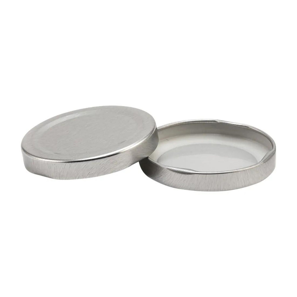 Two silver-colored, round metal lids designed for Gneiss Spice, featuring a slightly raised edge and smooth surface. One lid stands upright while the other lies flat, seamlessly integrating into their environment. These are replacement components labeled as "Unlabeled Lid" without magnetic components by Gneiss Spice.