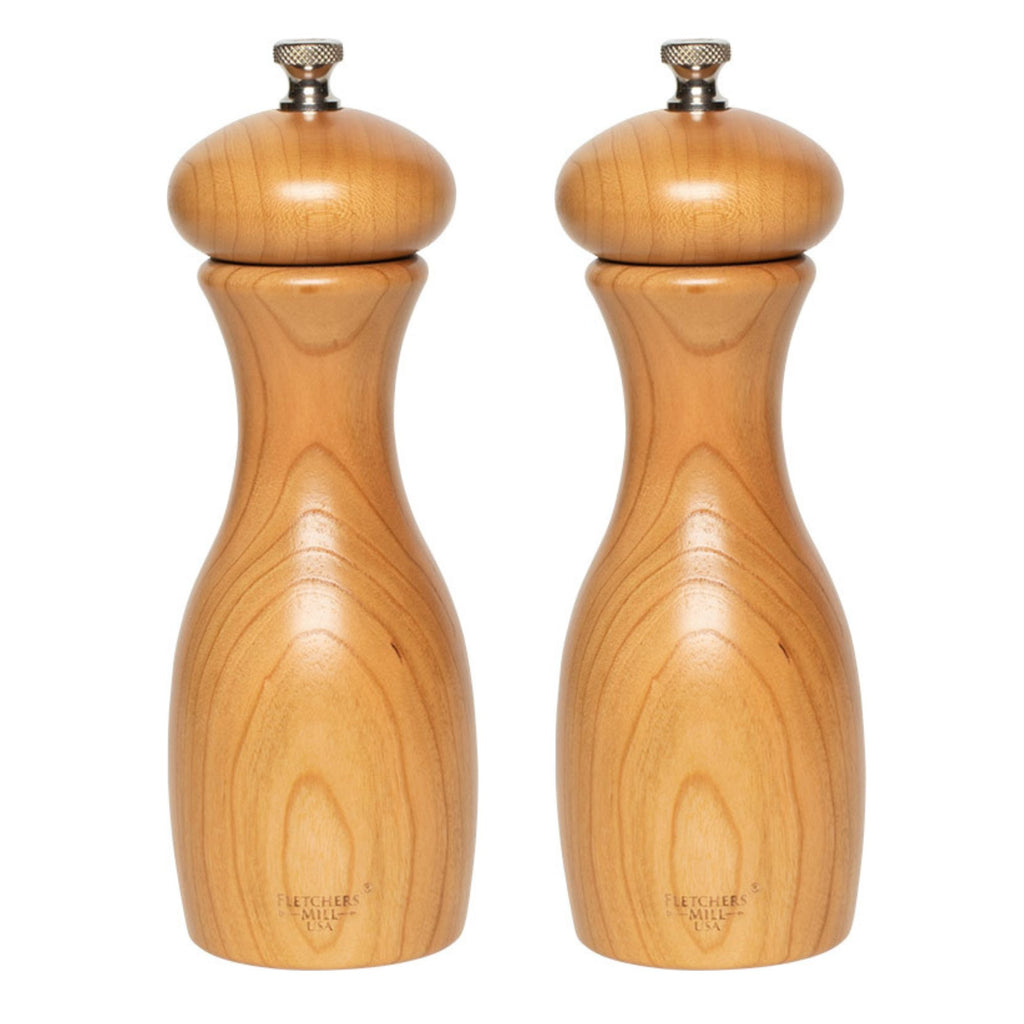 The Gneiss Spice Grinder Pair — Marsala Salt & Pepper Mill Set features two mills with a smooth, natural finish standing side by side. With durable craftsmanship and a classic, curvy shape, they are equipped with metal knobs on top for adjustable coarseness. The wood grain adds texture and warmth to their elegant design.