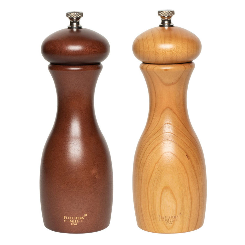 The Grinder Pair — Marsala Salt & Pepper Mill Set from Gneiss Spice showcases durable craftsmanship with two wooden pepper mills placed side by side. The mill on the left is a darker brown, and the one on the right has a lighter wood hue. Both are equipped with a metal knob on top and feature smooth, curved designs with adjustable coarseness to suit your grinding preference.