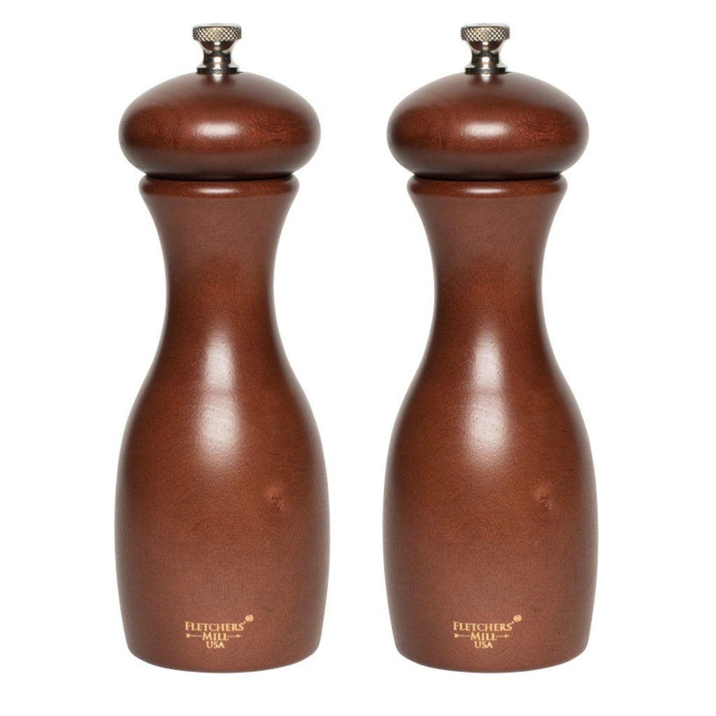 The Marsala Salt & Pepper Mill Set from Gneiss Spice features two wooden grinders with a smooth, polished finish, placed side by side. Each mill has adjustable coarseness and a rounded top, along with an engraved logo near the base, all set against a white background to highlight their durable craftsmanship.