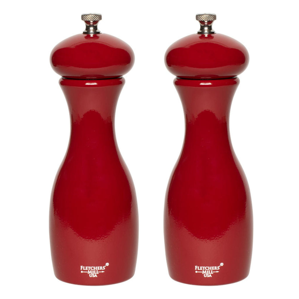 Two red pepper mills with metallic tops, featuring a glossy finish. These salt and pepper grinders from Gneiss Spice offer adjustable coarseness and are crafted from sustainably-harvested wood, with branding visible at the base. Included in "The Grinder Gift Set," the bundle comes with refills and a funnel.