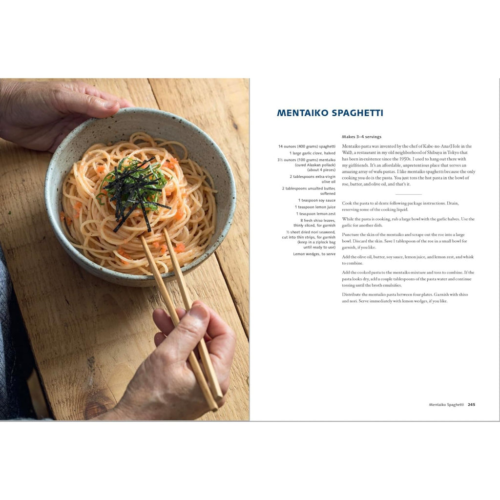 A person is holding a bowl of mentaiko spaghetti with chopsticks, highlighting an inventive take on fusion cuisine inspired by Japan. The garnished spaghetti rests appealingly on a wooden surface. To the right, adventurous home cooks can discover this delightful recipe in "Wafu Cooking: Everyday Recipes with Japanese Style" by Gneiss Spice.