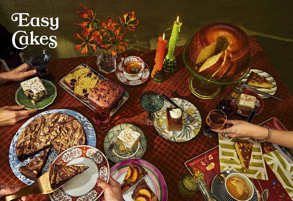 A table adorned with cakes and desserts, featuring a bundt cake, chocolate cake, and loaf cake from the beloved cookbook "What's For Dessert: Simple Recipes for Dessert People" by Gneiss Spice. Three hands reach for slices amidst candles, flowers, and tea cups. "Easy Cakes" text graces the top left corner.