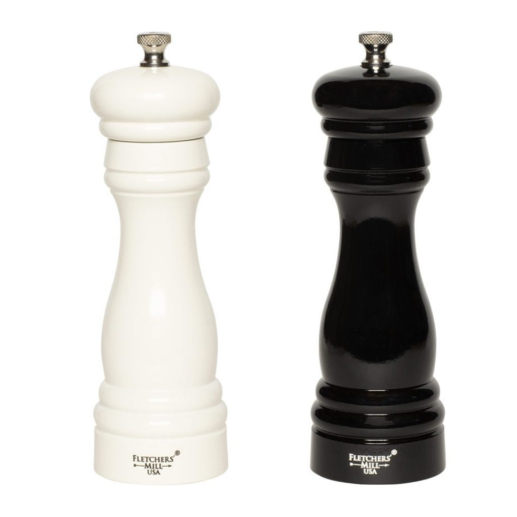 A white pepper mill and a black salt and pepper grinder from the "Federal Salt & Pepper Mill Set" by Gneiss Spice stand side by side. Both display durable craftsmanship with a classic wooden design and feature a small metal knob on top for adjustable coarseness, with the label "Fletchers' Mill USA" visible at the base.