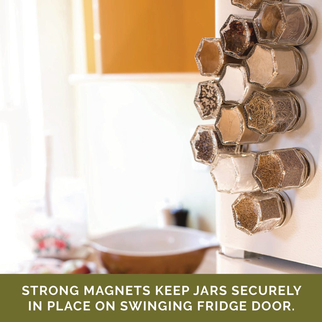 The hexagonal magnetic spice jars from Gneiss Spice, filled with organic spices, are securely attached to the refrigerator door. Text reads, "BASICS | 12 magnetic jars have strong magnets that keep them firmly in place on swinging fridge doors." The kitchen space is blurred in the background.