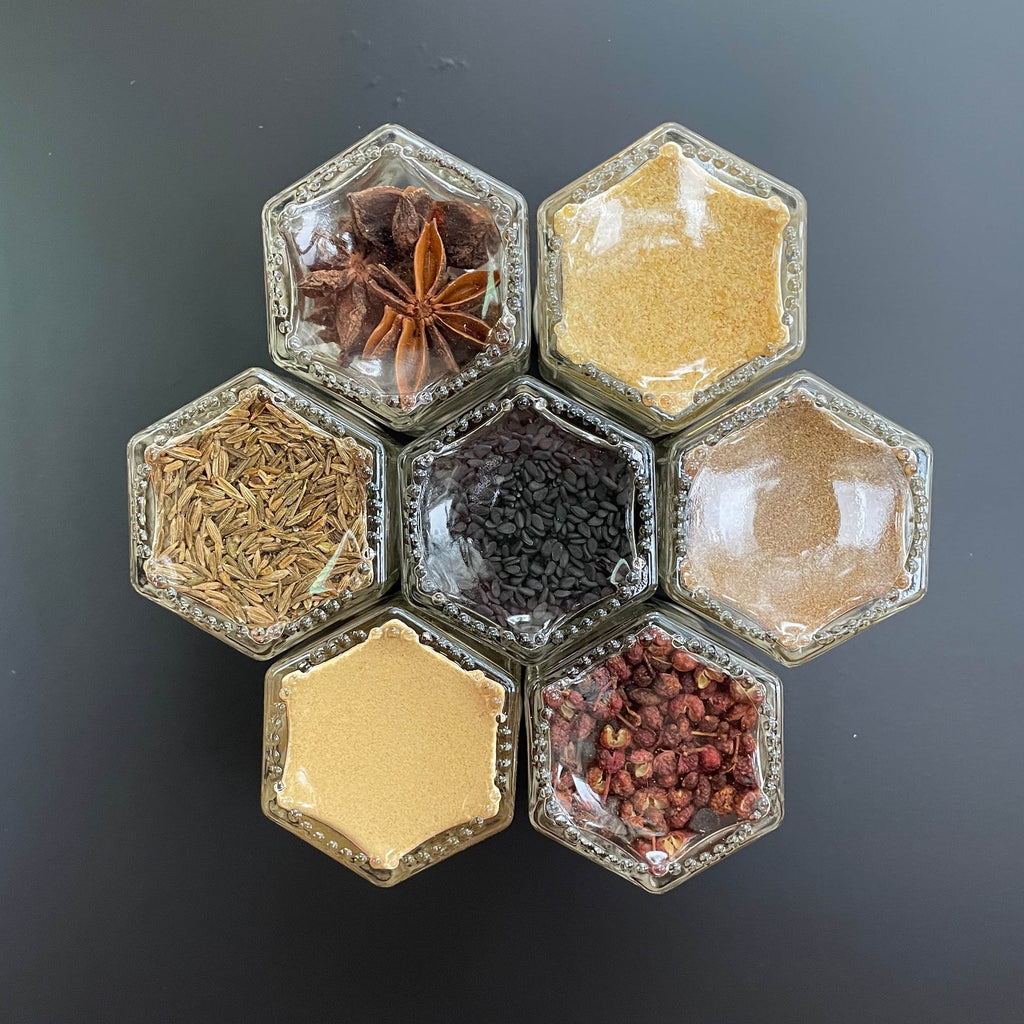 The Sichuan Spice Kit by Gneiss Spice features organic spices, including star anise, cumin seeds, and black sesame seeds, in hexagonal glass jars. Perfect for adding authenticity and depth to your dishes.