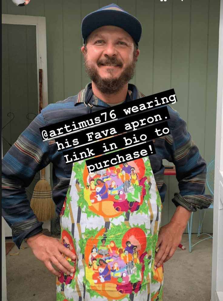 A person smiles on a porch in a colorful apron displaying Joelle Avellino illustrations. Text overlay: "@artimus76 wearing his Gneiss Spice Limited Edition Fava apron. Link in bio to purchase!.