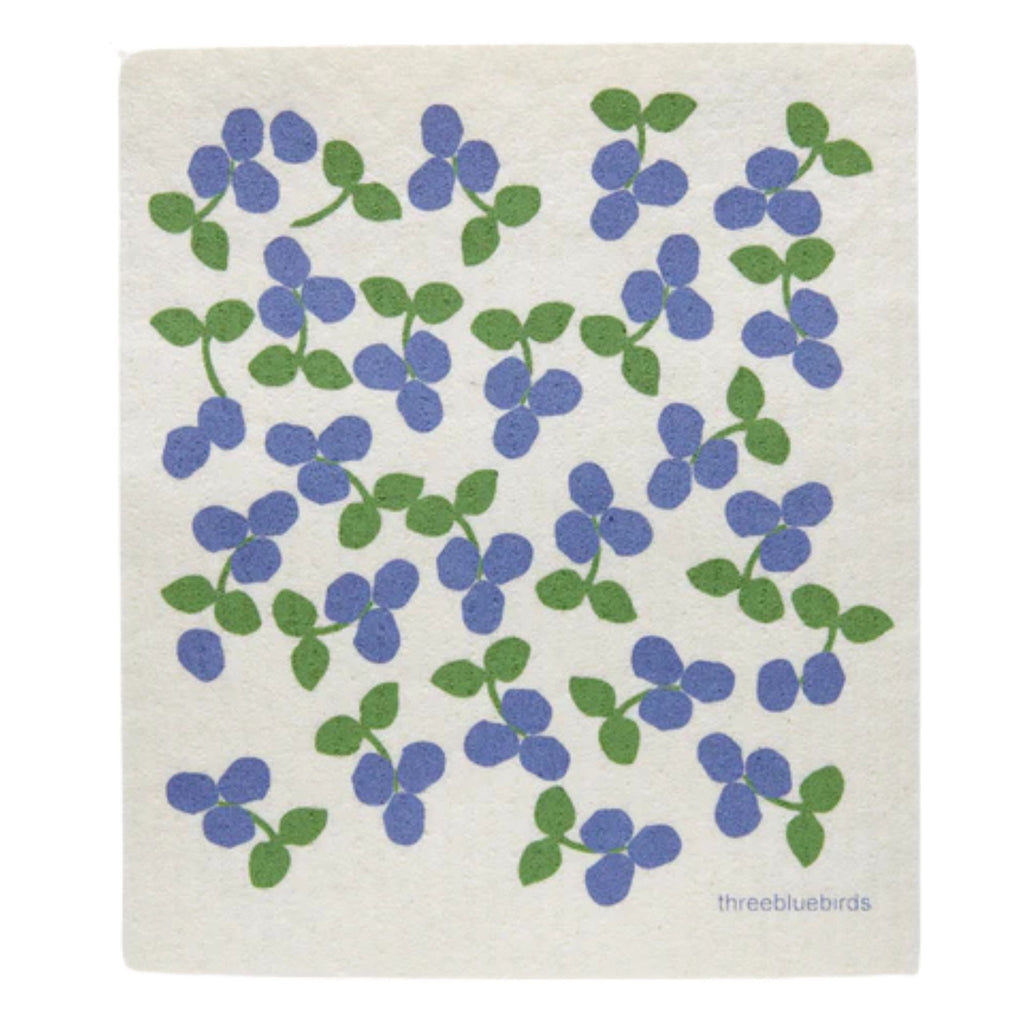 A stylish and sustainable Swedish Dishcloth from Gneiss Spice showcases a pattern of purple flowers and green leaves on a white background. The words "threebluebirds" appear in the bottom right corner, offering an eco-friendly solution for your home. Don't miss the promotion: buy 3 and get 1 free!