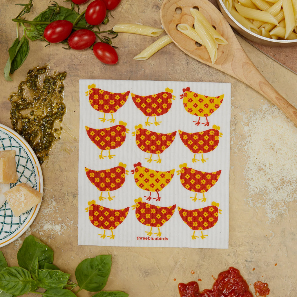 A charming Swedish Dishcloth from Gneiss Spice, featuring red and yellow floral chicken patterns, enhances your kitchen’s aesthetic. Accompanied by cherry tomatoes, penne pasta, basil, cheese, and tomato sauce on a rustic surface, it's an eco-friendly choice for every culinary artist. Plus, take advantage of our promotion: buy three and get one free!