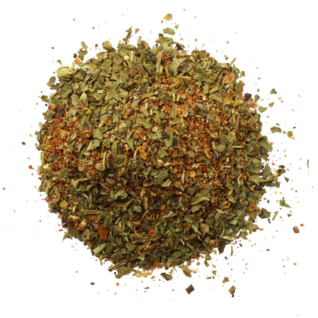 A heap of Mexican Herbs by Gneiss Spice, showcasing a blend of green leaves and reddish-brown pieces, is spread on a white background, offering a subtle smoky flavor.