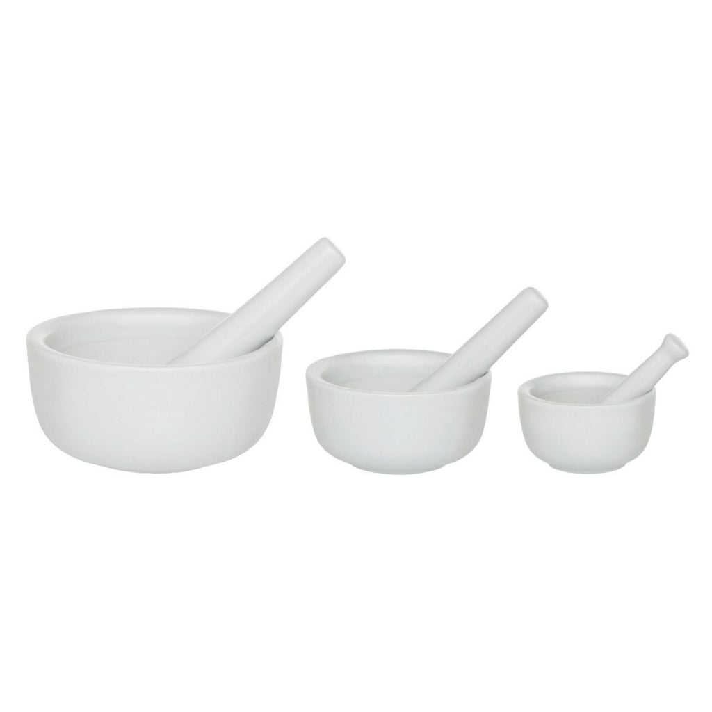 The arrangement features three Gneiss Spice mortar and pestle kitchen tool sets, crafted from white porcelain. Lined up from left to right in descending size order, they form an ideal setup for grinding spices against a plain white backdrop.