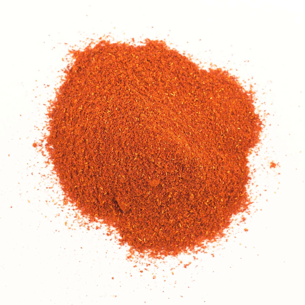 A pile of Gneiss Spice's organic Spanish Paprika is spread out on a white surface. This paprika has a finely textured appearance, showcasing a rich, deep red color with a hint of smoky flavor.