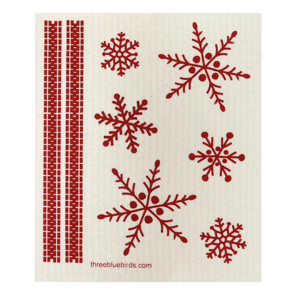 A decorative dishcloth from Gneiss Spice, titled "Swedish Dishcloth — Merry & Bright," showcases two red vertical stripes on the left and an array of red snowflake patterns in various sizes on the right. This eco-friendly and sustainable solution features the website "threebluebirds.com" printed in small red font at the bottom.