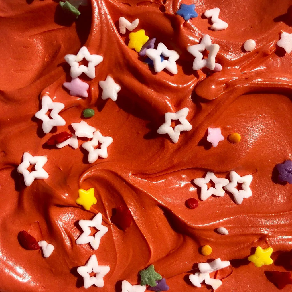 Close-up of smooth, swirled red frosting adorned with Gneiss Spice's Sprinkles—All-Natural Starfetti, featuring vibrant star-shaped hues of white, yellow, pink, and purple, creating a festive and playful texture.