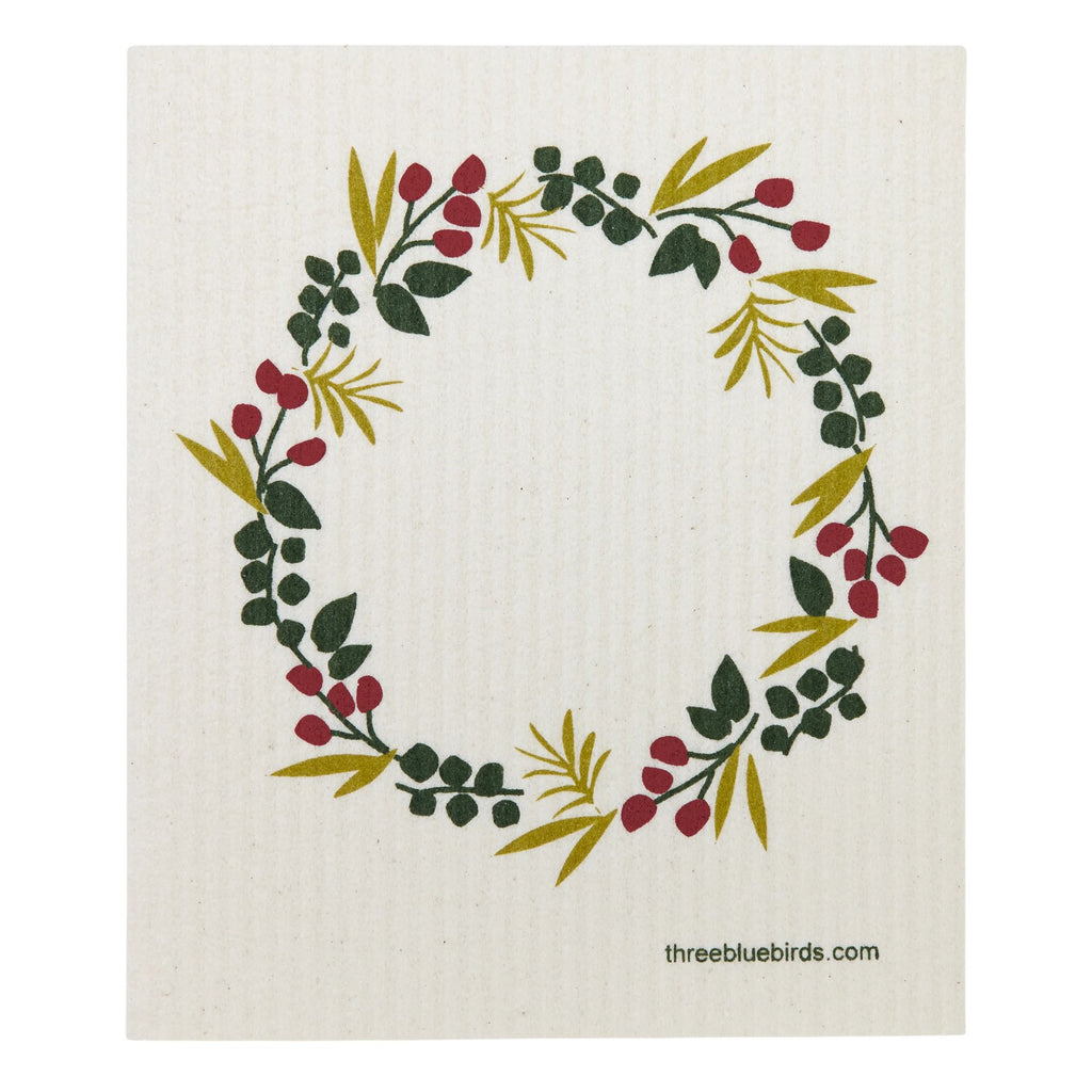 Introducing the Swedish Dishcloth — Winter Wreath by Gneiss Spice, featuring a decorative circular wreath design with vibrant green leaves and red berries on a beige background. This eco-friendly cloth combines beauty and sustainability for your kitchen needs, with "threebluebirds.com" printed at the bottom.